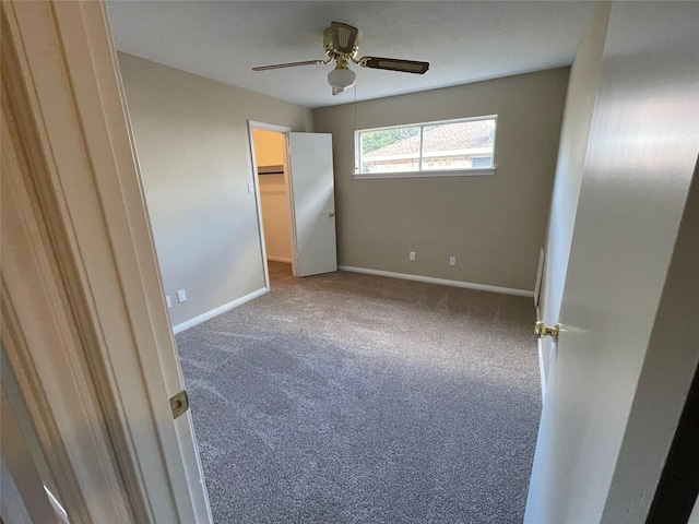 unfurnished bedroom featuring carpet floors, ceiling fan, baseboards, and a walk in closet