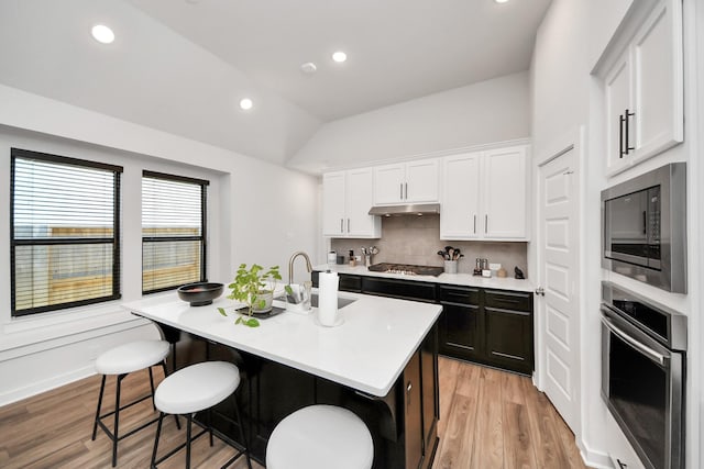 kitchen with a center island with sink, a kitchen breakfast bar, stainless steel appliances, light countertops, and a sink