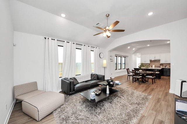 living room with lofted ceiling, arched walkways, light wood-style flooring, visible vents, and a ceiling fan