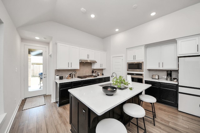 kitchen featuring under cabinet range hood, stainless steel appliances, a sink, white cabinets, and a kitchen bar