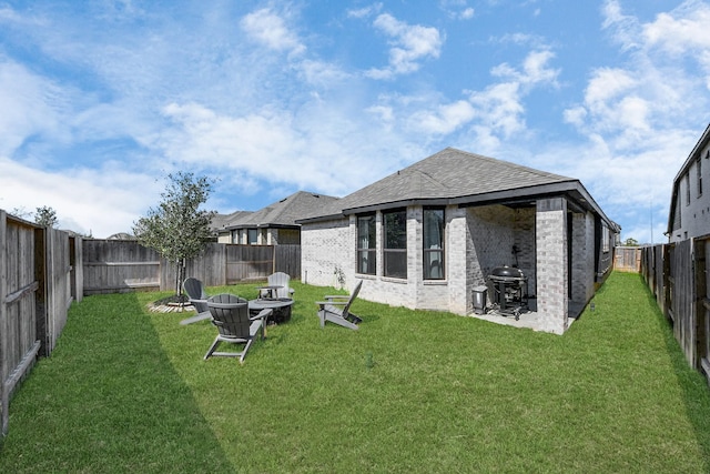 back of property featuring a yard, a fenced backyard, a fire pit, and brick siding