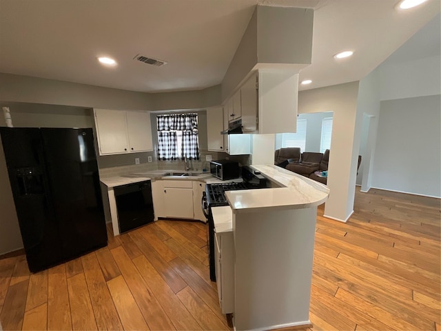 kitchen featuring light countertops, a peninsula, black appliances, and light wood finished floors