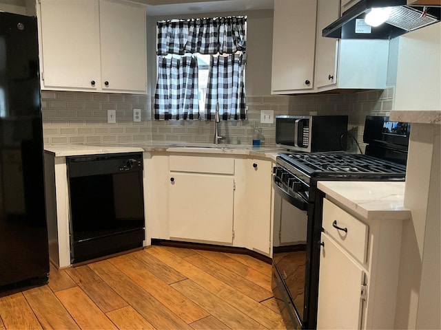 kitchen featuring light countertops, light wood-style floors, a sink, under cabinet range hood, and black appliances