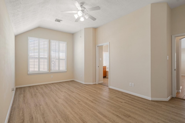 interior space featuring a textured ceiling, vaulted ceiling, light wood-type flooring, and baseboards