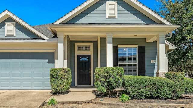 doorway to property with concrete driveway, a shingled roof, a porch, and an attached garage