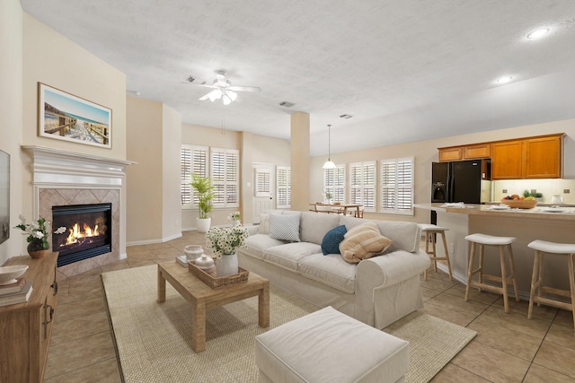 living area featuring light tile patterned floors, a tile fireplace, a ceiling fan, and baseboards