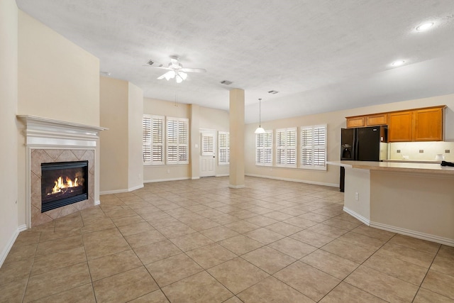 unfurnished living room with light tile patterned floors, plenty of natural light, ceiling fan, and a tile fireplace