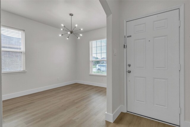 entryway with baseboards, an inviting chandelier, and light wood-style floors