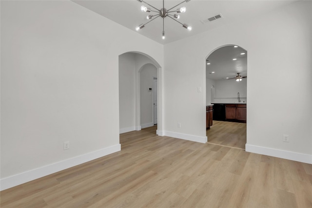 empty room featuring light wood-type flooring, baseboards, visible vents, and arched walkways