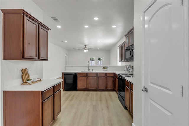 kitchen featuring visible vents, light wood-style flooring, a peninsula, black appliances, and a sink