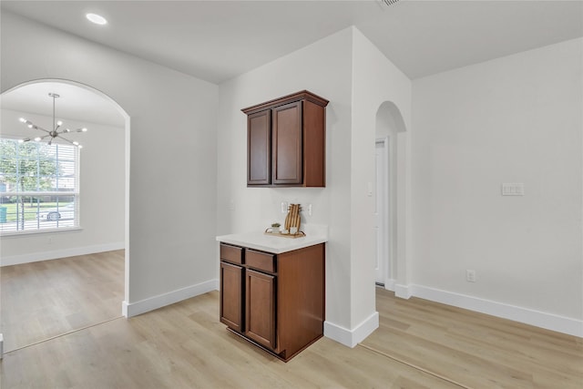 interior space with baseboards, arched walkways, light countertops, light wood-type flooring, and a notable chandelier