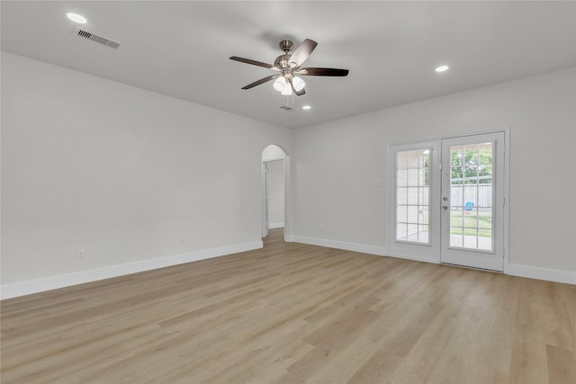 empty room featuring arched walkways, light wood-type flooring, visible vents, and baseboards