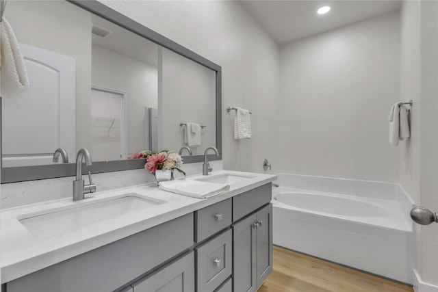 full bathroom with a garden tub, double vanity, wood finished floors, and a sink