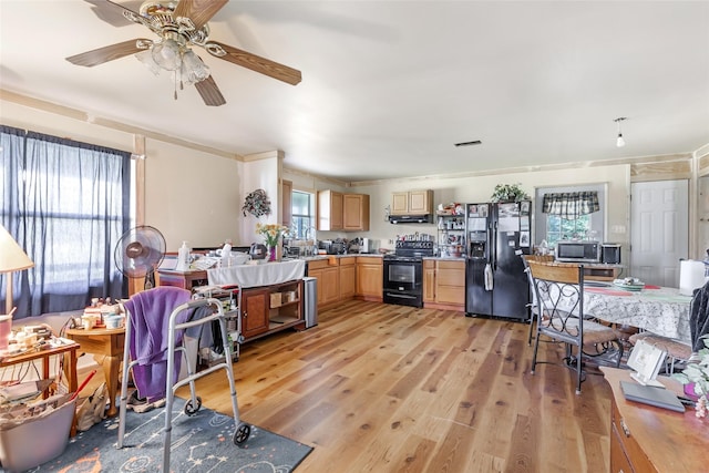 kitchen with a sink, light countertops, light brown cabinetry, light wood-type flooring, and black appliances