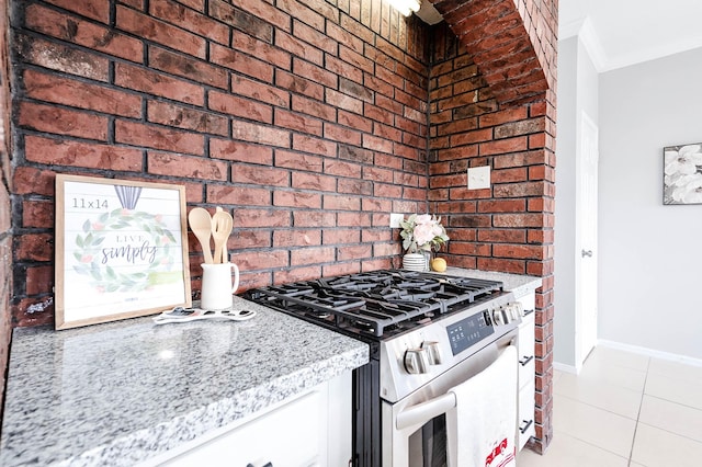 kitchen featuring light tile patterned floors, white cabinets, baseboards, stainless steel gas range, and light stone countertops