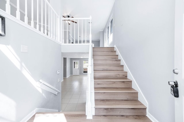 stairway featuring baseboards, a towering ceiling, and tile patterned floors