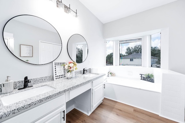 bathroom featuring double vanity, a sink, a bath, and wood finished floors