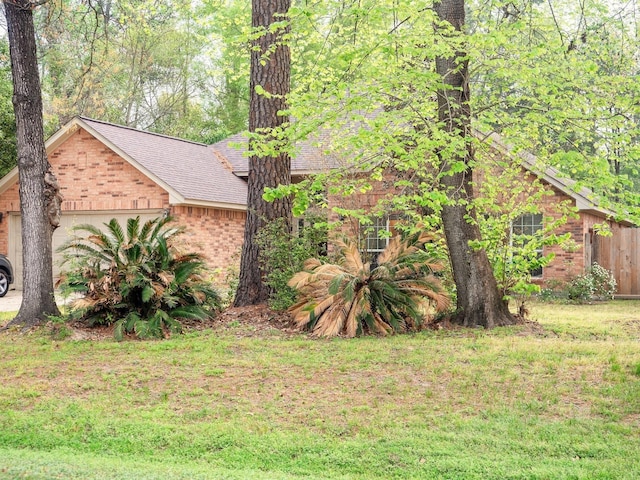 view of side of home with a garage, a yard, brick siding, and a shingled roof