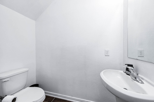 half bath with vaulted ceiling, toilet, baseboards, and a sink