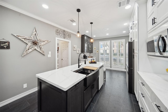 kitchen featuring ornamental molding, visible vents, a center island with sink, dark cabinetry, and a sink