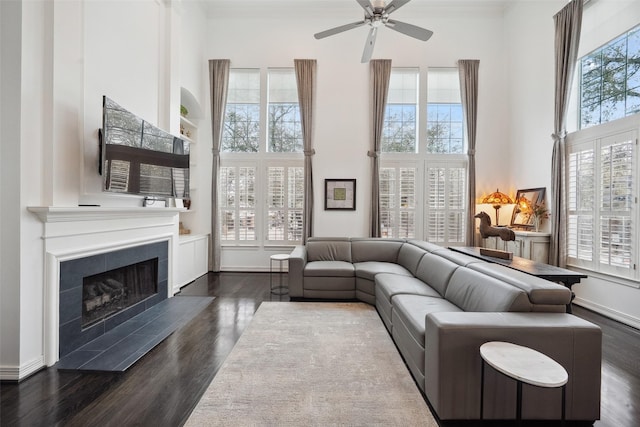 living area featuring a ceiling fan, dark wood finished floors, a fireplace, baseboards, and a towering ceiling