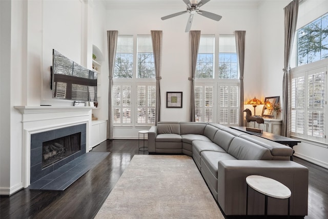 living room with a tiled fireplace, dark wood-style floors, a high ceiling, a ceiling fan, and crown molding