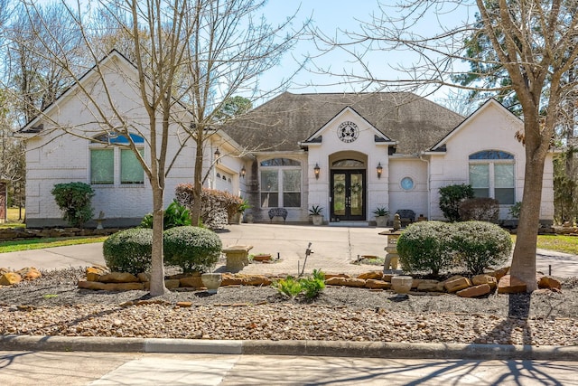 french provincial home featuring brick siding, french doors, a shingled roof, and concrete driveway