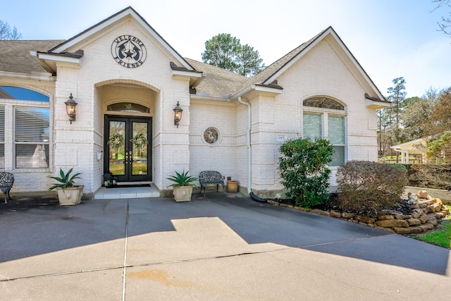 entrance to property with brick siding, roof with shingles, and french doors