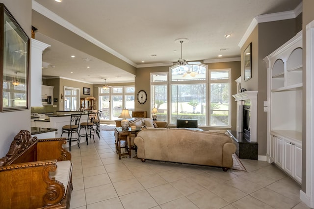 living area featuring a fireplace with raised hearth, light tile patterned flooring, recessed lighting, a ceiling fan, and crown molding