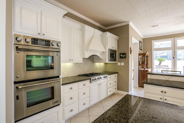 kitchen featuring light tile patterned floors, white cabinets, appliances with stainless steel finishes, ornamental molding, and decorative backsplash