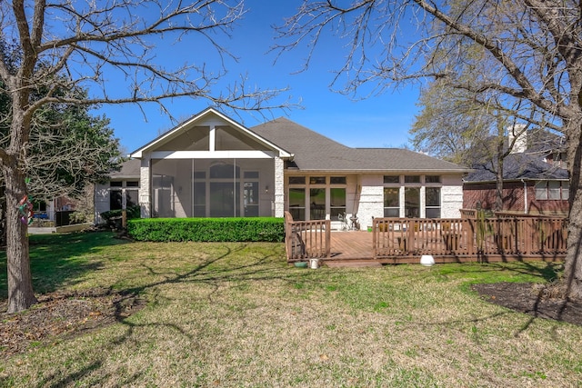 rear view of house with a shingled roof, a lawn, a sunroom, a deck, and brick siding