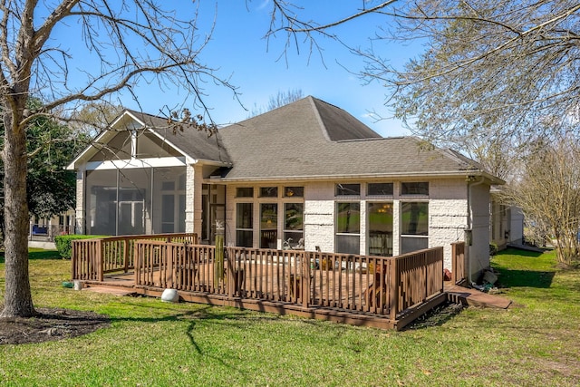 back of property featuring a sunroom, a wooden deck, brick siding, and a yard