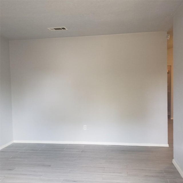 spare room featuring wood finished floors, visible vents, and baseboards