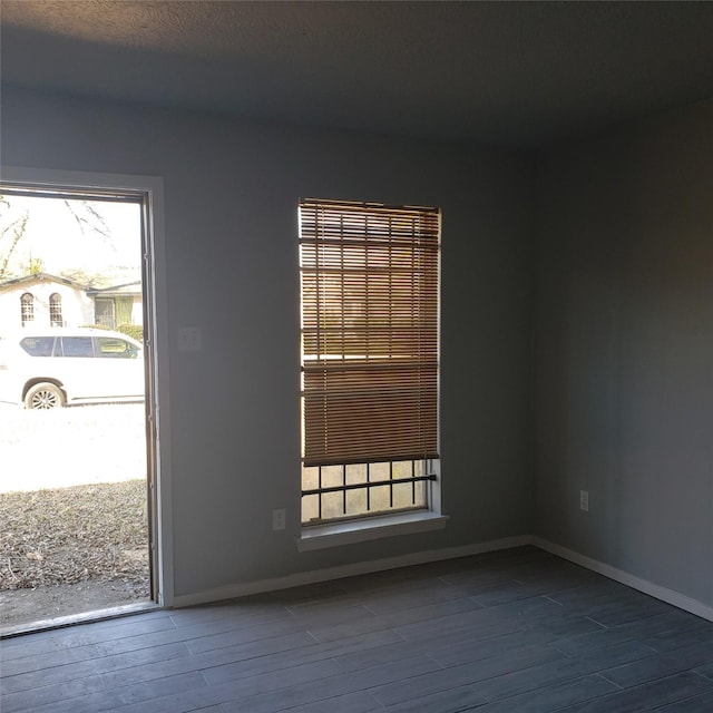 spare room featuring dark wood-type flooring, plenty of natural light, and baseboards