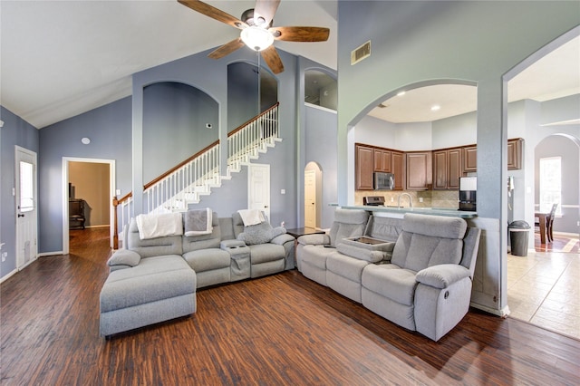 living area featuring arched walkways, high vaulted ceiling, stairway, and visible vents