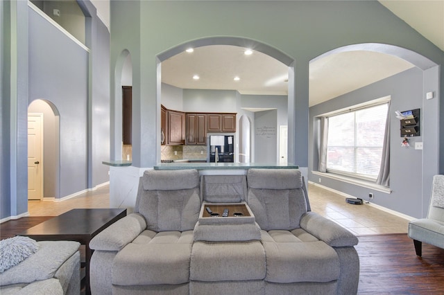 living area featuring arched walkways, recessed lighting, a towering ceiling, light wood-style floors, and baseboards