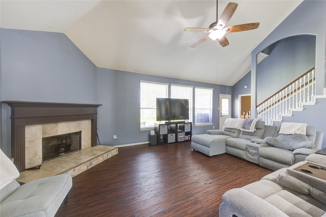 living area with a tile fireplace, ceiling fan, stairway, wood finished floors, and vaulted ceiling