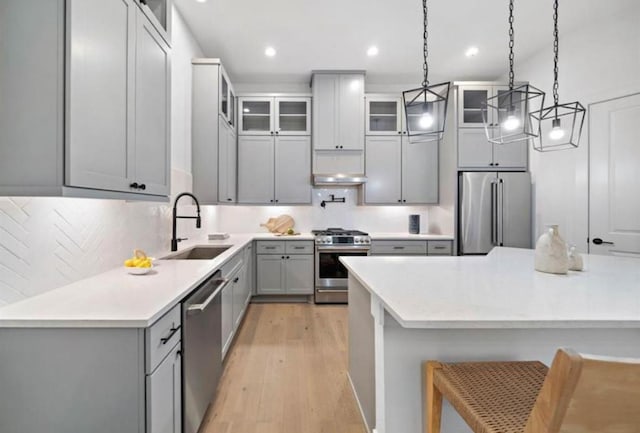 kitchen featuring light wood finished floors, stainless steel appliances, gray cabinets, a sink, and a kitchen bar