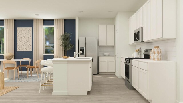 kitchen with white cabinets, light wood finished floors, a kitchen island with sink, and stainless steel appliances