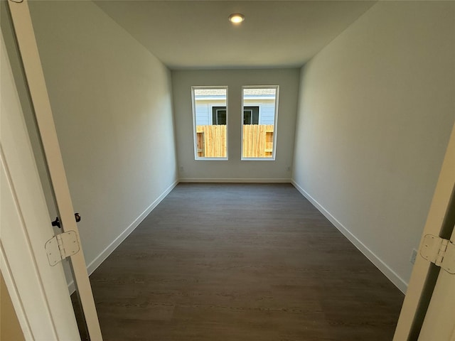 empty room with baseboards and dark wood-type flooring