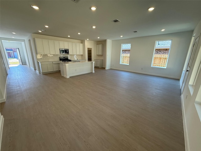 kitchen featuring a center island with sink, decorative backsplash, appliances with stainless steel finishes, open floor plan, and light wood-style floors