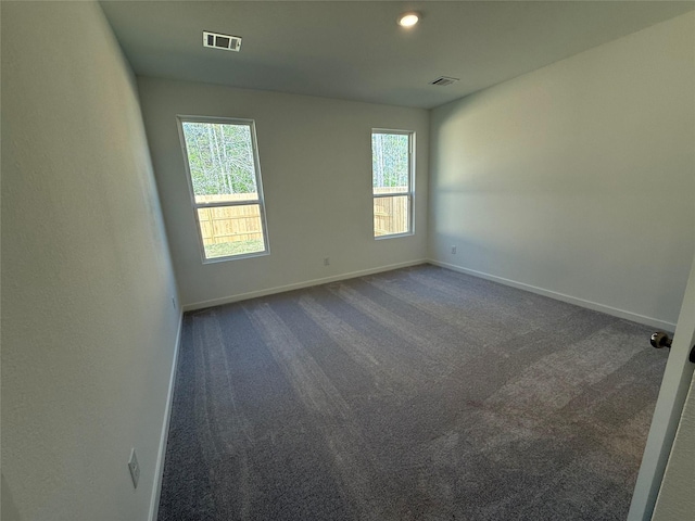 unfurnished room with dark colored carpet, visible vents, and baseboards