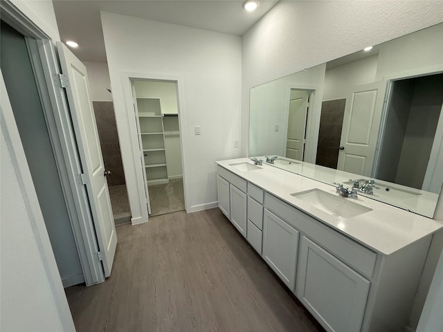 bathroom with double vanity, baseboards, a sink, and wood finished floors