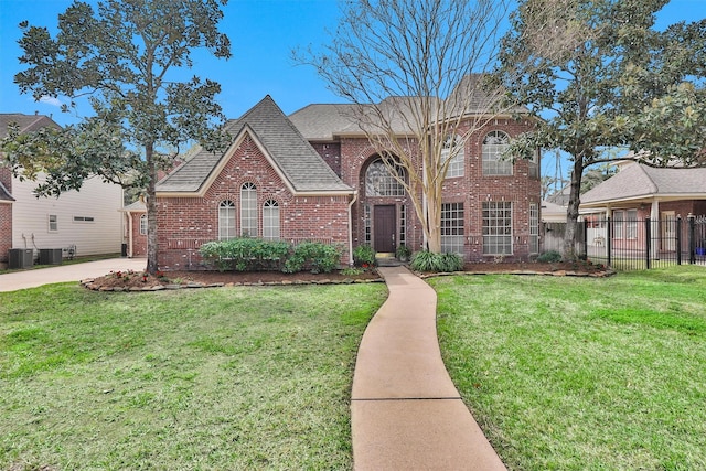 traditional-style house with brick siding, central air condition unit, a shingled roof, a front yard, and fence