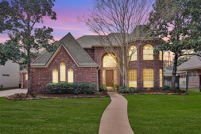 view of front of house featuring fence, a lawn, and brick siding