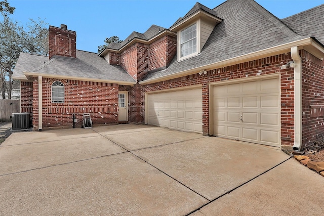 exterior space featuring driveway, a garage, a shingled roof, central AC, and brick siding