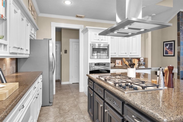 kitchen with white cabinetry, ornamental molding, appliances with stainless steel finishes, dark stone counters, and island exhaust hood