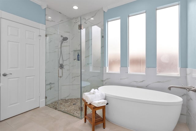 bathroom with a freestanding tub, a marble finish shower, a wealth of natural light, and tile walls