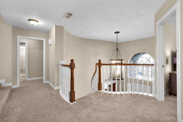 hallway featuring carpet floors, baseboards, visible vents, and an upstairs landing