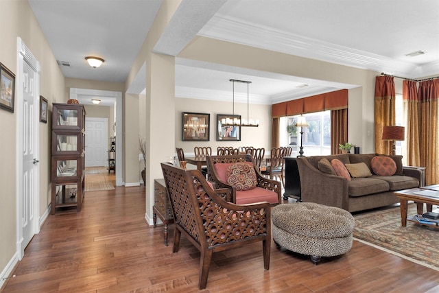 living area with baseboards, visible vents, wood finished floors, crown molding, and a notable chandelier